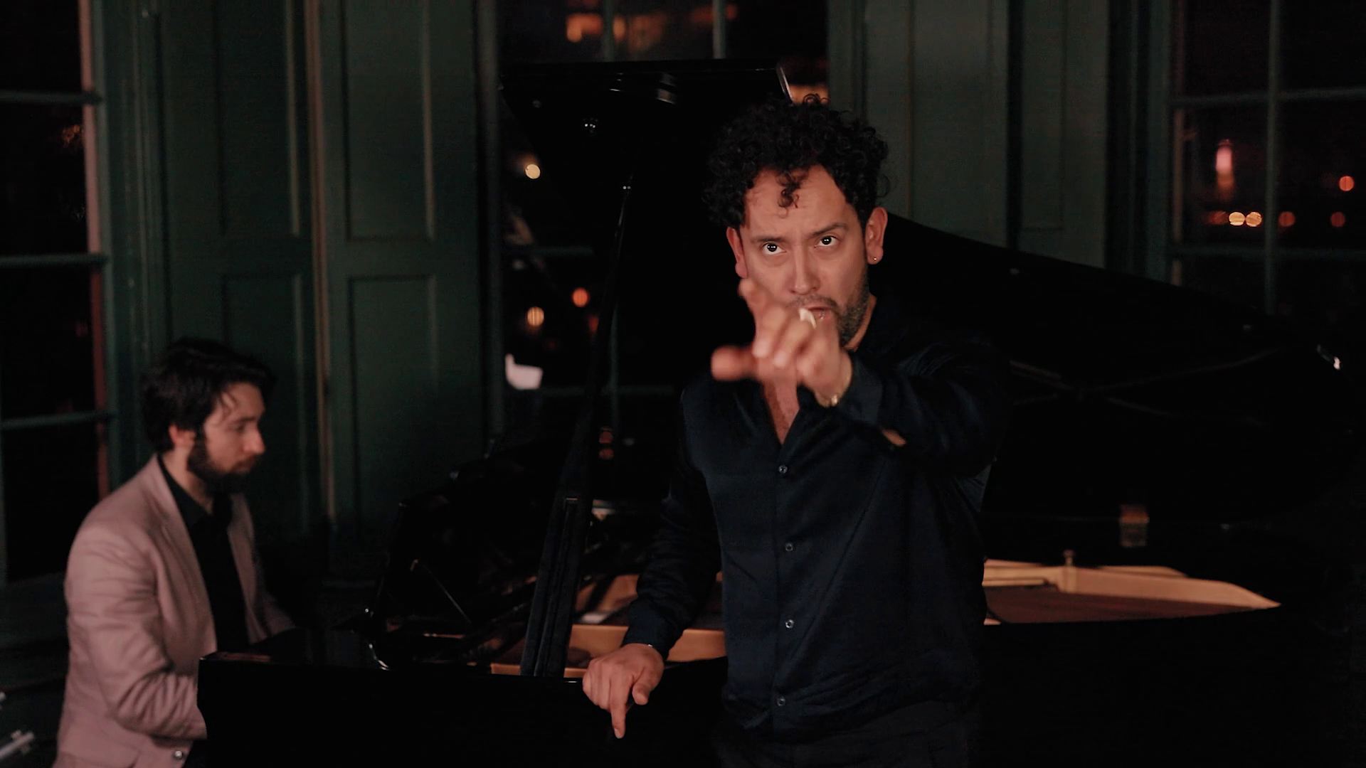Conductor directing a rehearsal, pianist in the background